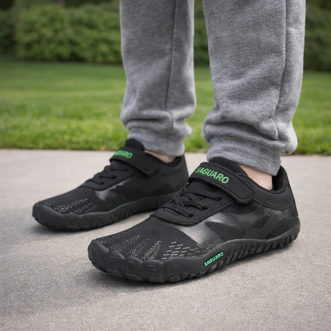 Zapatillas anchas infantiles negras con malla transpirable para actividad física escolar.